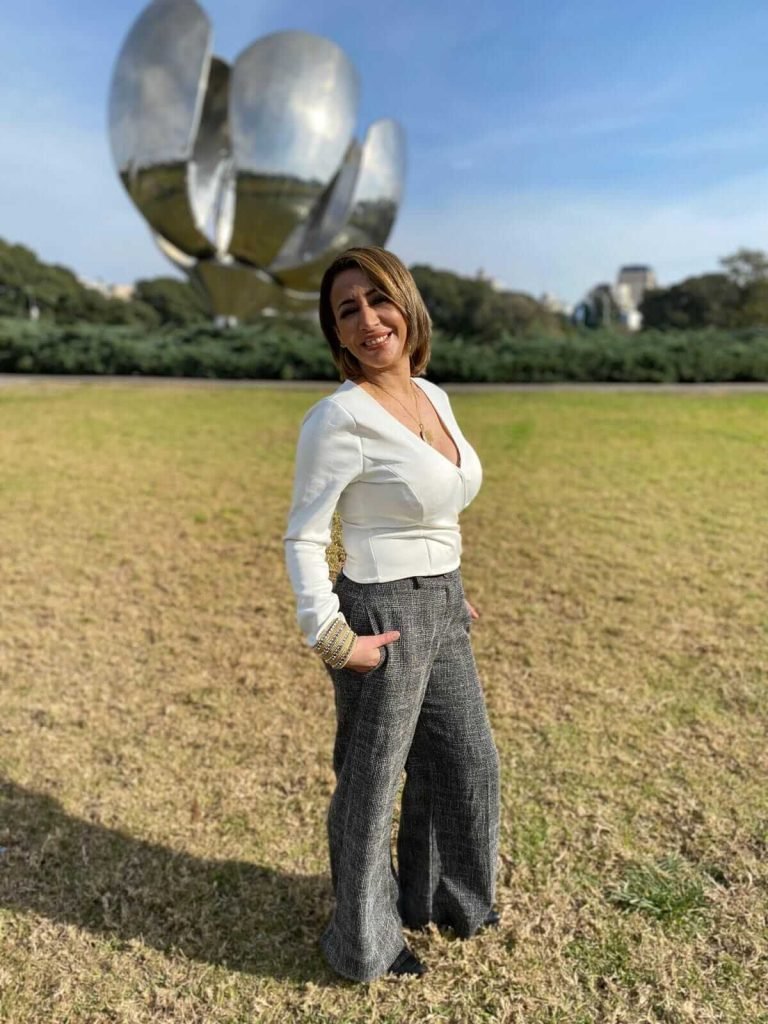 Mujer posando frente a la escultura Floralis Genérica con cielo azul y campo verde al fondo en Buenos Aires